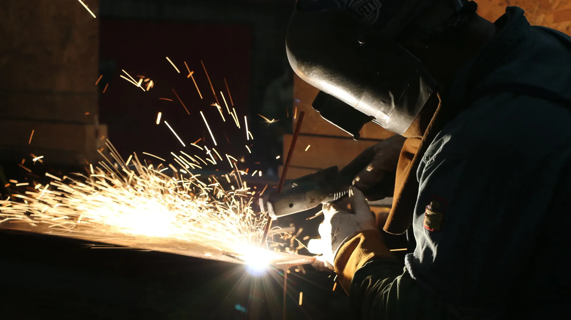 A worker in a welding helmet, sparks flying in a dark workshop